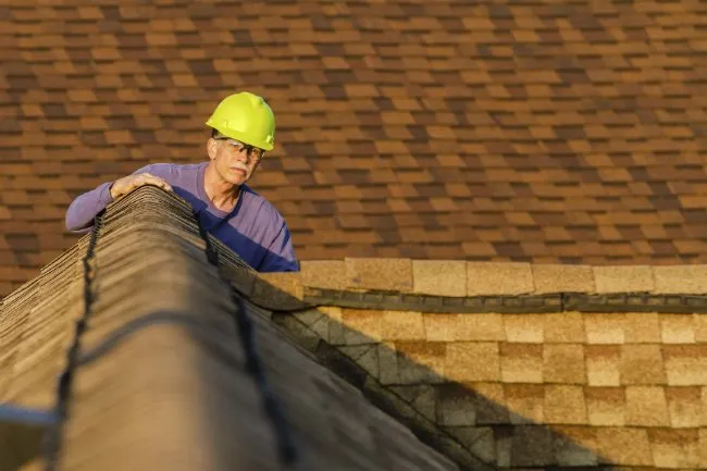 Roofing contractor inspecting the ridge of a shingle roof